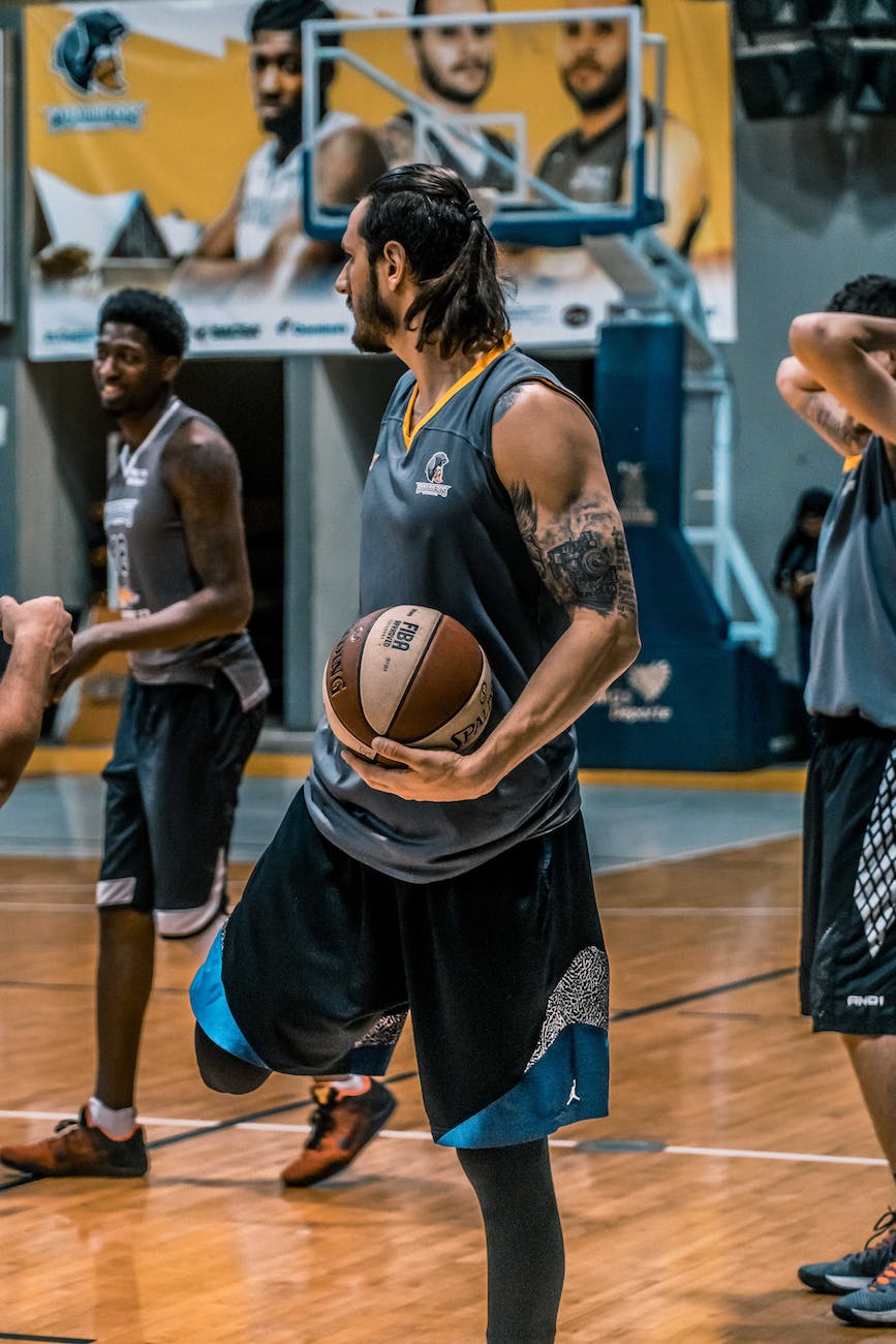 man in gray sleeveless shirt carrying white and brown spalding basketball